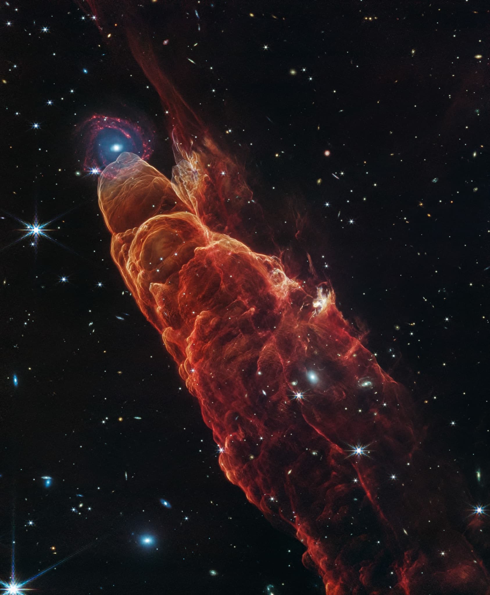 Webb view of the cosmic tornado, a glowing herbig-haro outflow beside a distant galaxy.