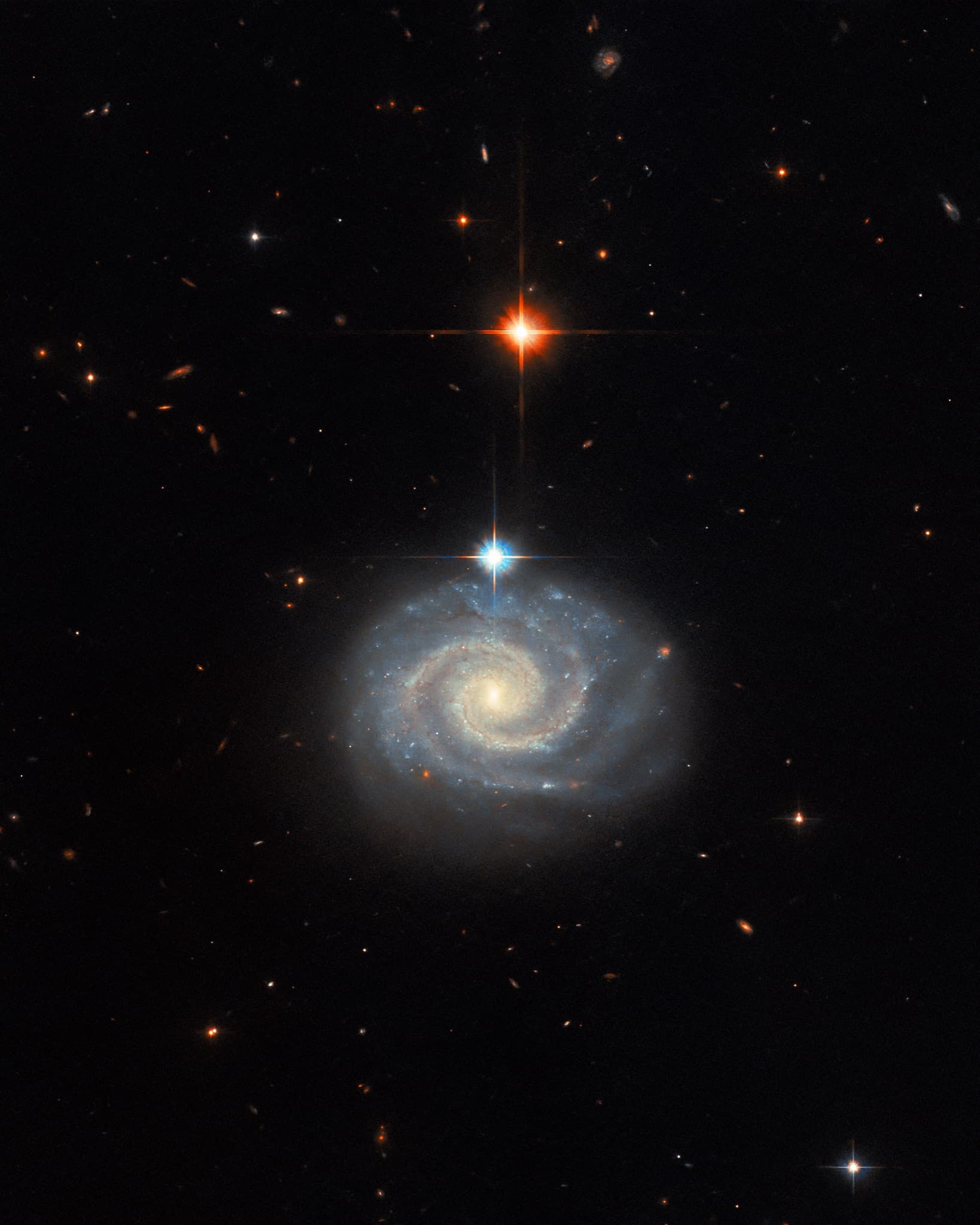 The spiral galaxy MCG-01-24-014 seen nearly face-on, its energetic active galactic nucleus glowing at the center of softly lit spiral arms.