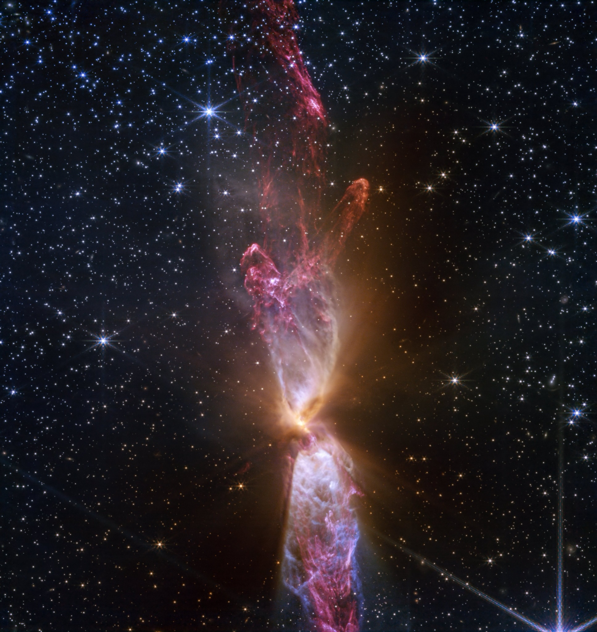 Webb detail of an actively forming star system with bright outflows and dark dust lanes.