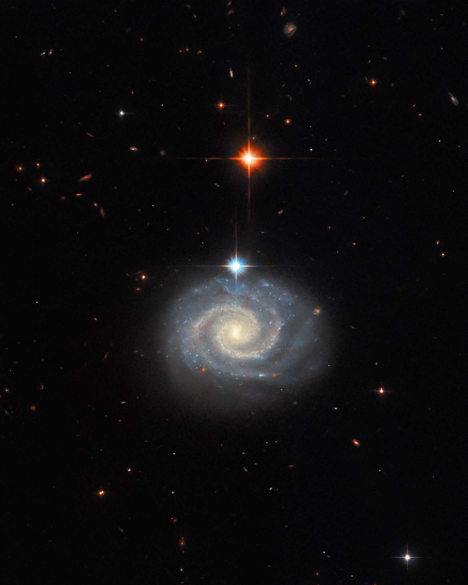 The spiral galaxy MCG-01-24-014 seen nearly face-on, its energetic active galactic nucleus glowing at the center of softly lit spiral arms.